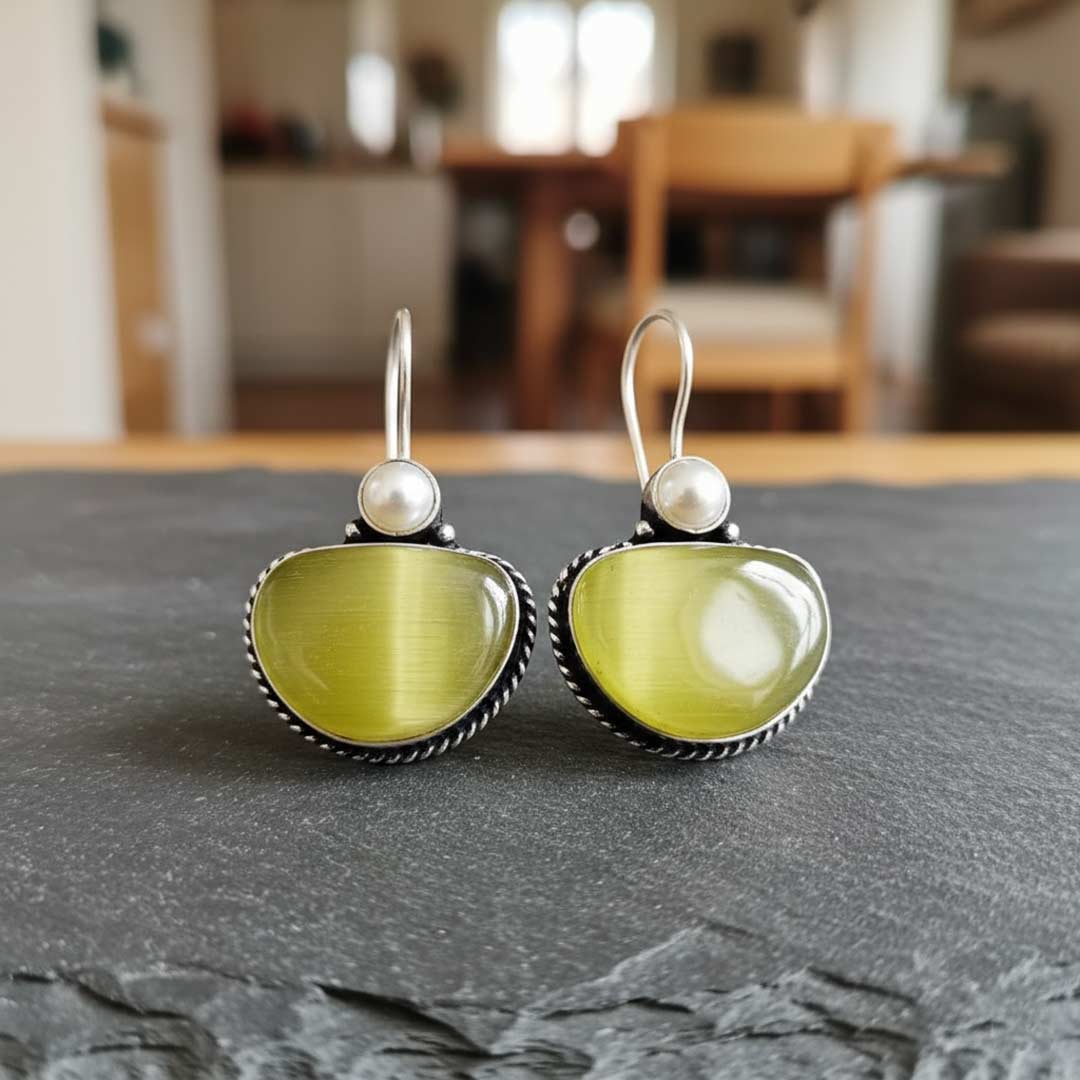 Pair of earrings with green stones and pearl-like centers on a gray surface.