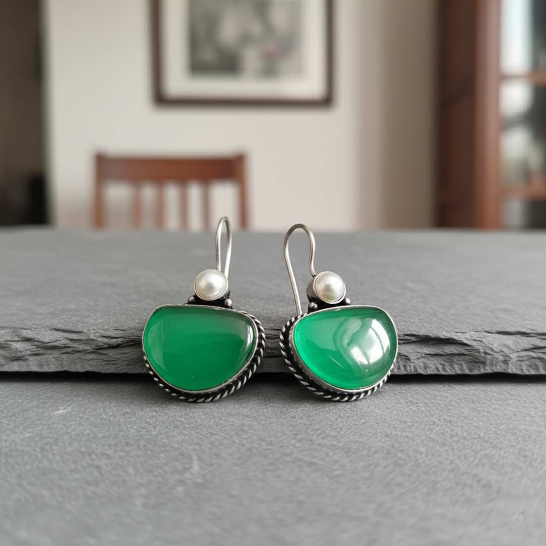 Green earrings with pearl accents on a gray surface