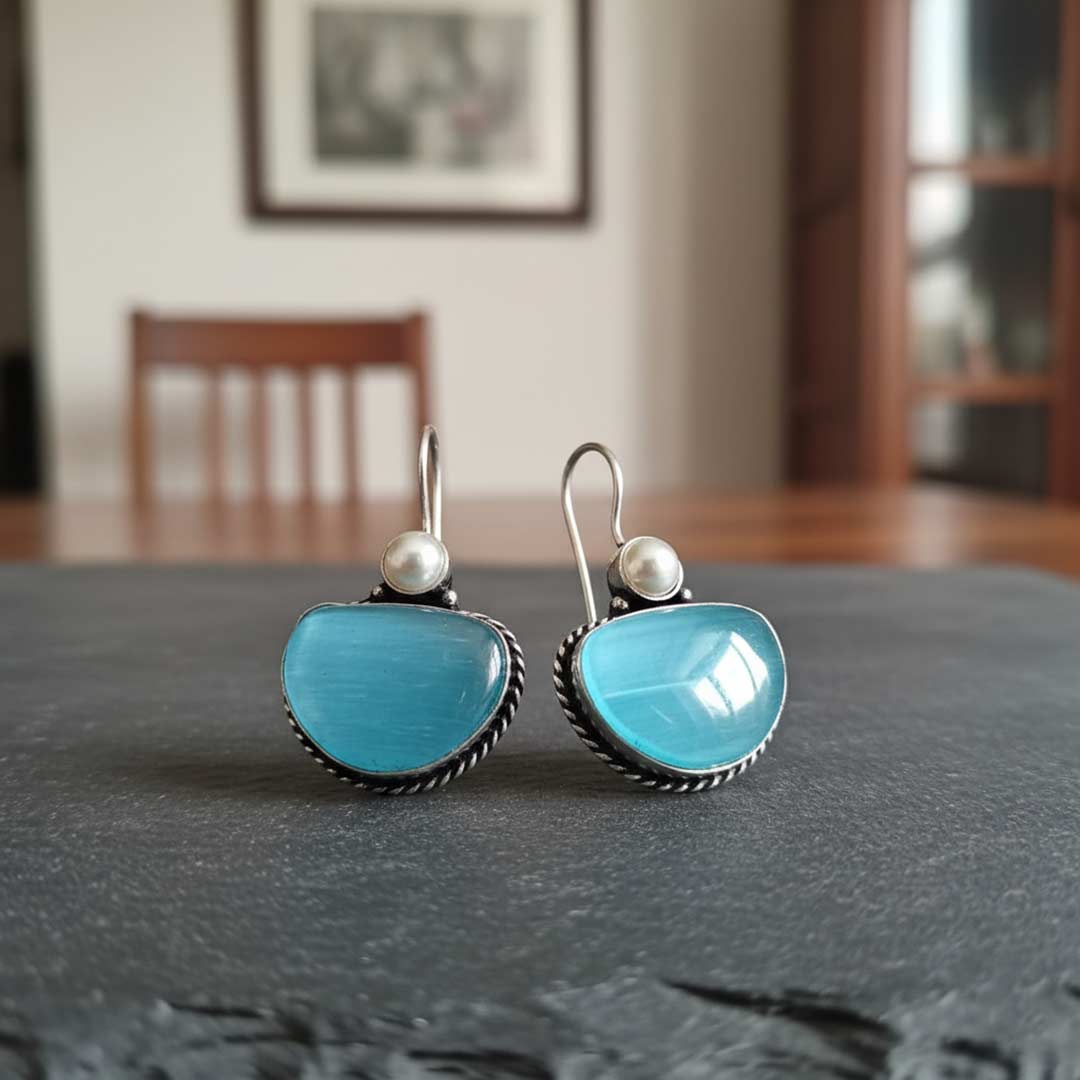 Turquoise earrings with pearl accents on a dark surface, blurred indoor background