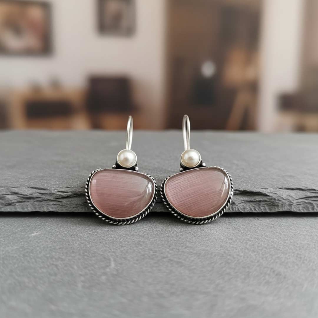 Pair of earrings with pink stones and pearl centers on a gray surface.