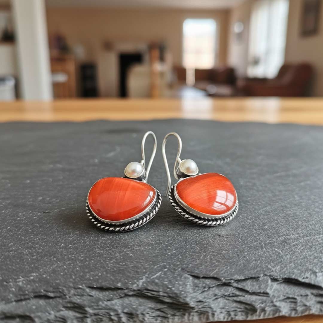 Pair of earrings with orange stones and silver hooks on a dark surface.