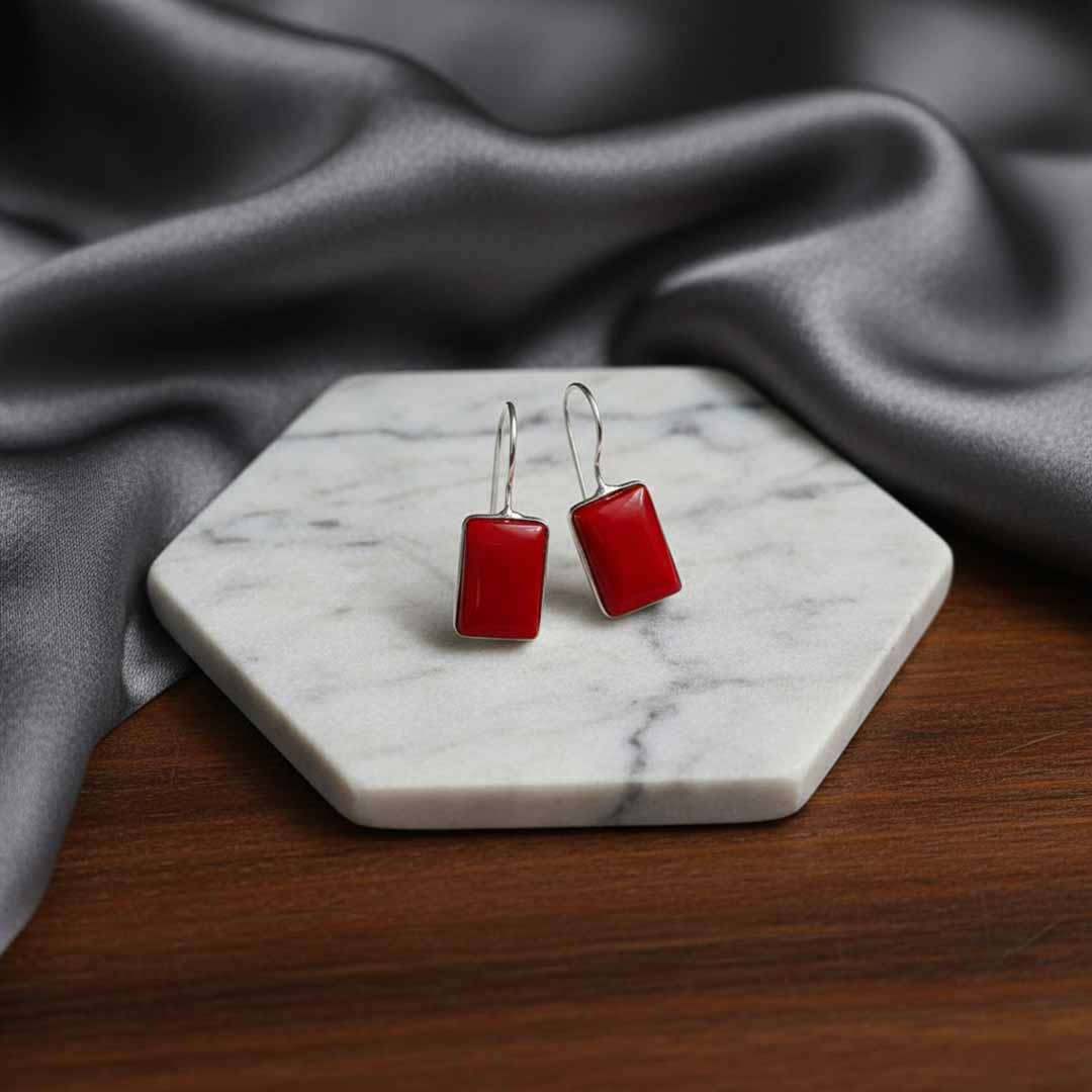 Red square earrings on a marble stand with gray fabric in the background