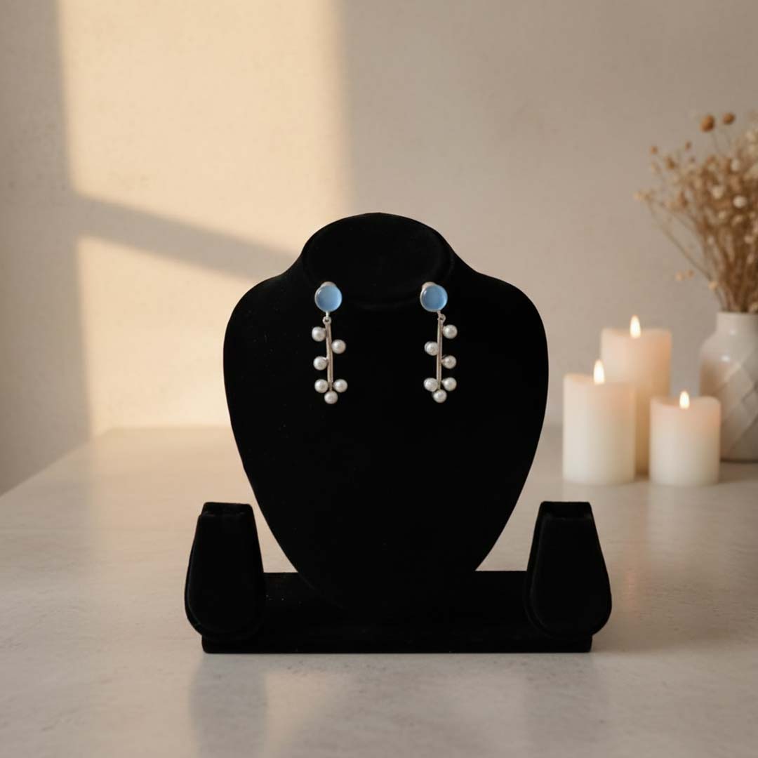 Pair of earrings on a black velvet stand with candles and decor in the background