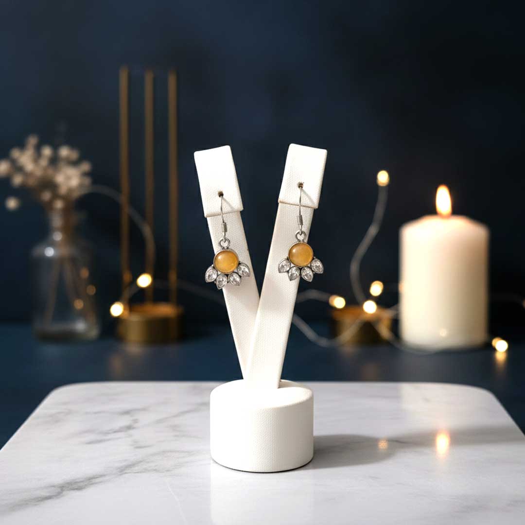 Pair of earrings on a white stand with a candle and decorative items in the background