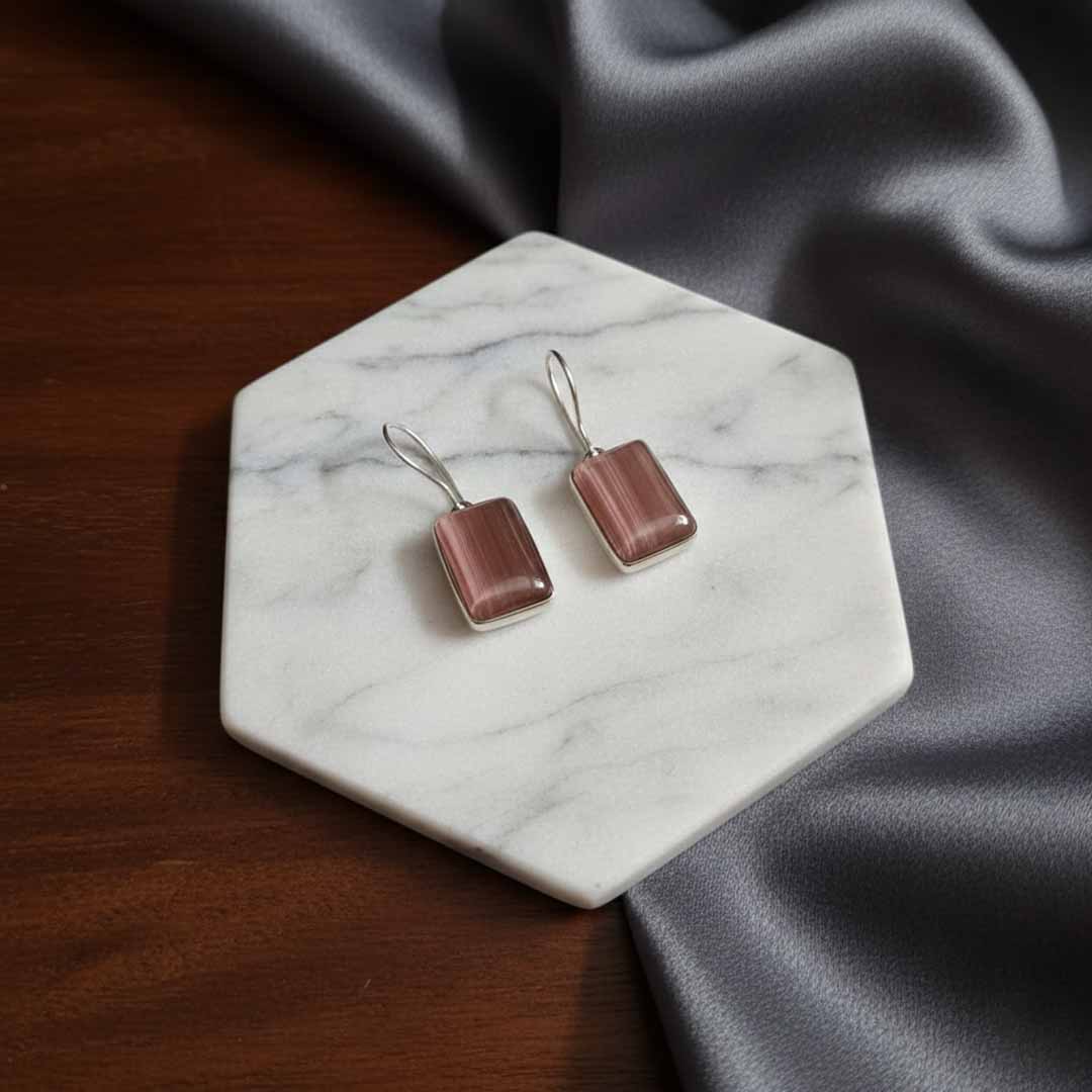 Pair of earrings on a marble coaster with fabric background