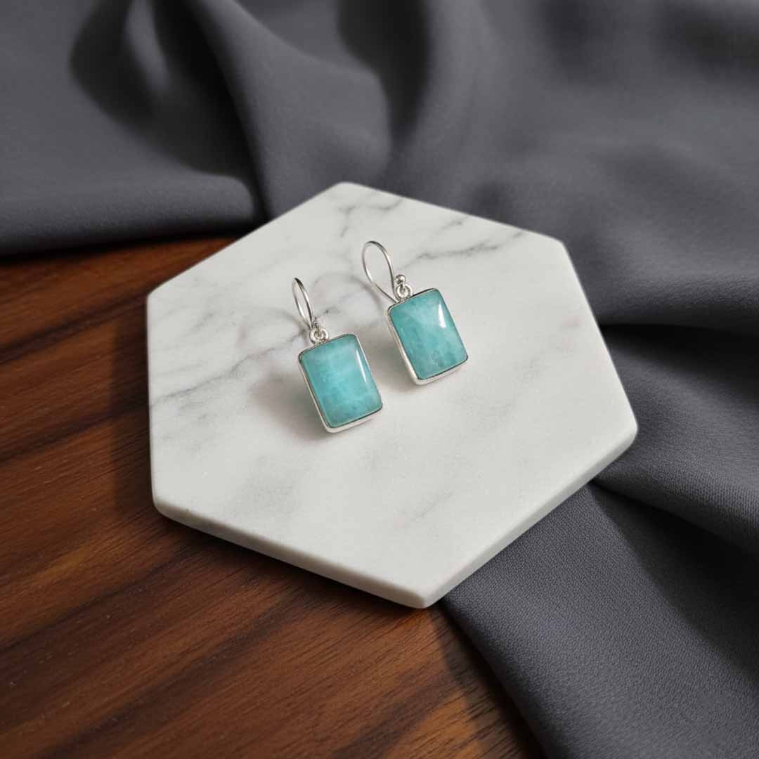 Turquoise square earrings on a marble stand with a gray fabric background