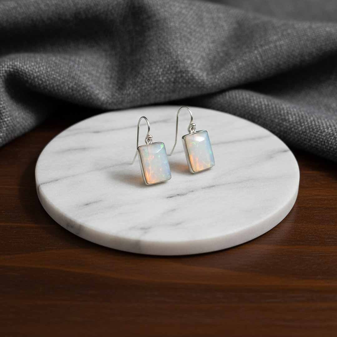 Opal earrings on a marble stand with gray fabric in the background