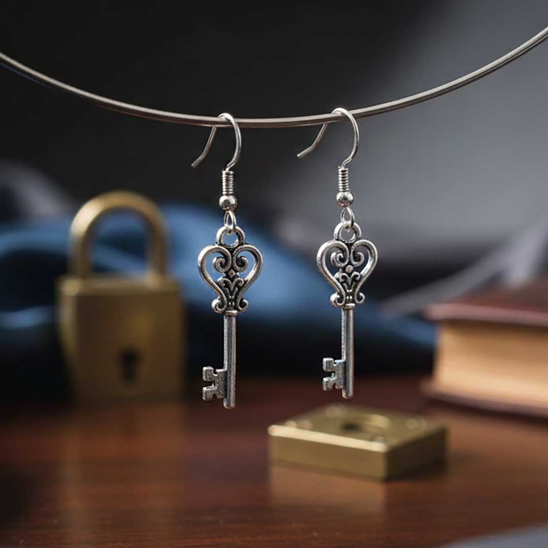 Silver key-shaped earrings hanging on a wire against a blurred background with books and a lock.