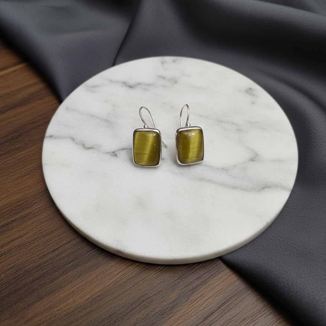 Pair of gold square earrings on a marble coaster with gray fabric background