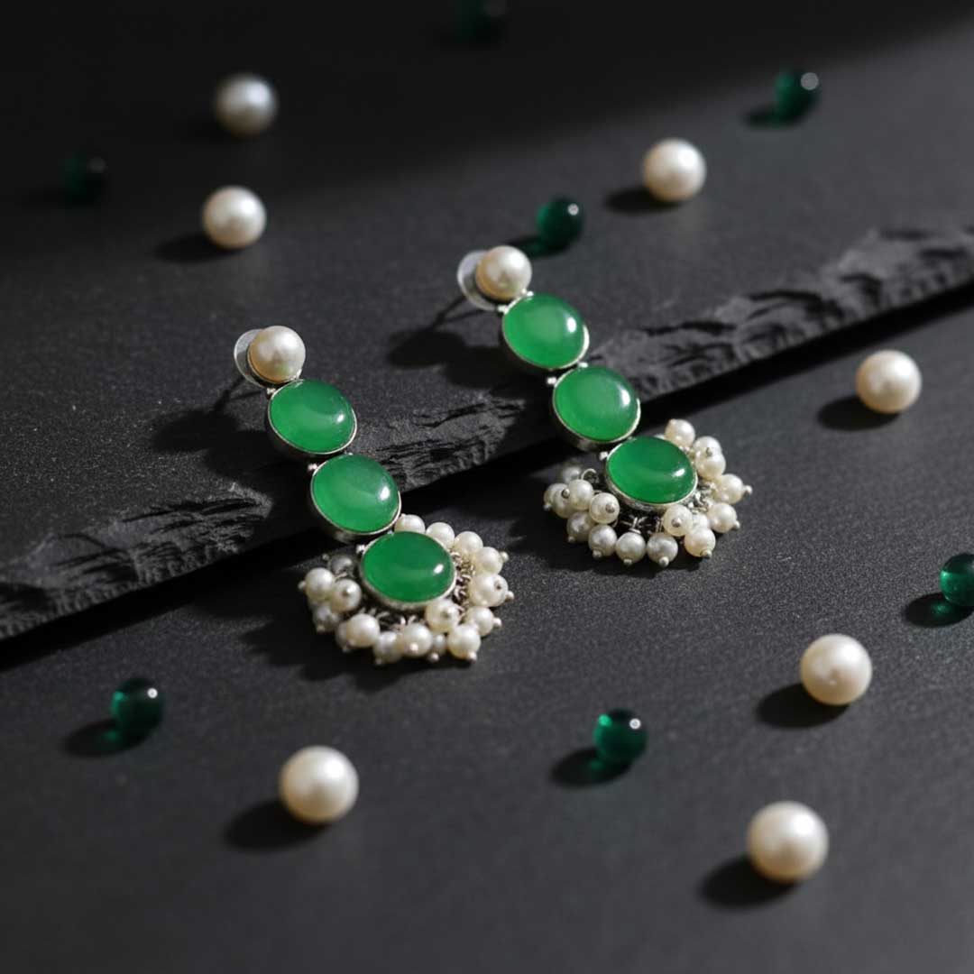 Pair of earrings with green gemstones and pearl accents on a dark surface.