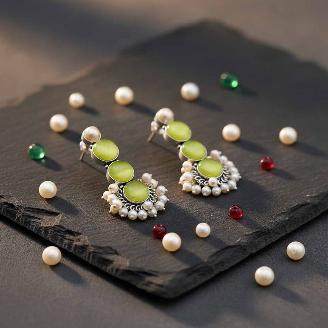 Pair of earrings with green stones and pearl-like accents on a dark surface.