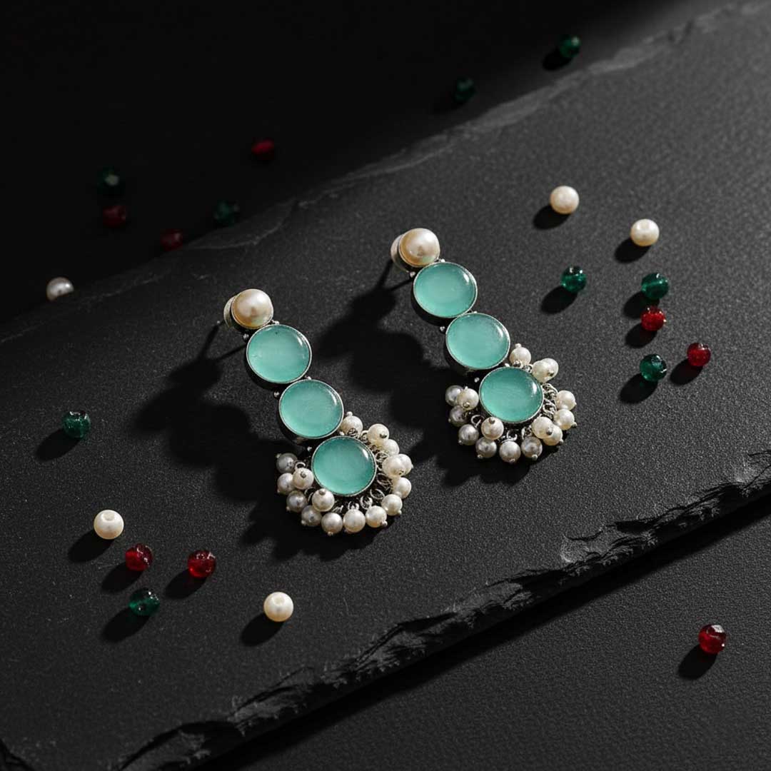 Pair of turquoise earrings with pearl accents on a dark surface with scattered gemstones.