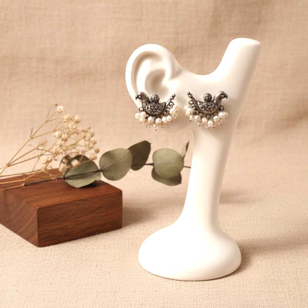 Pair of earrings on a white stand with a wooden box and dried flowers on a beige background