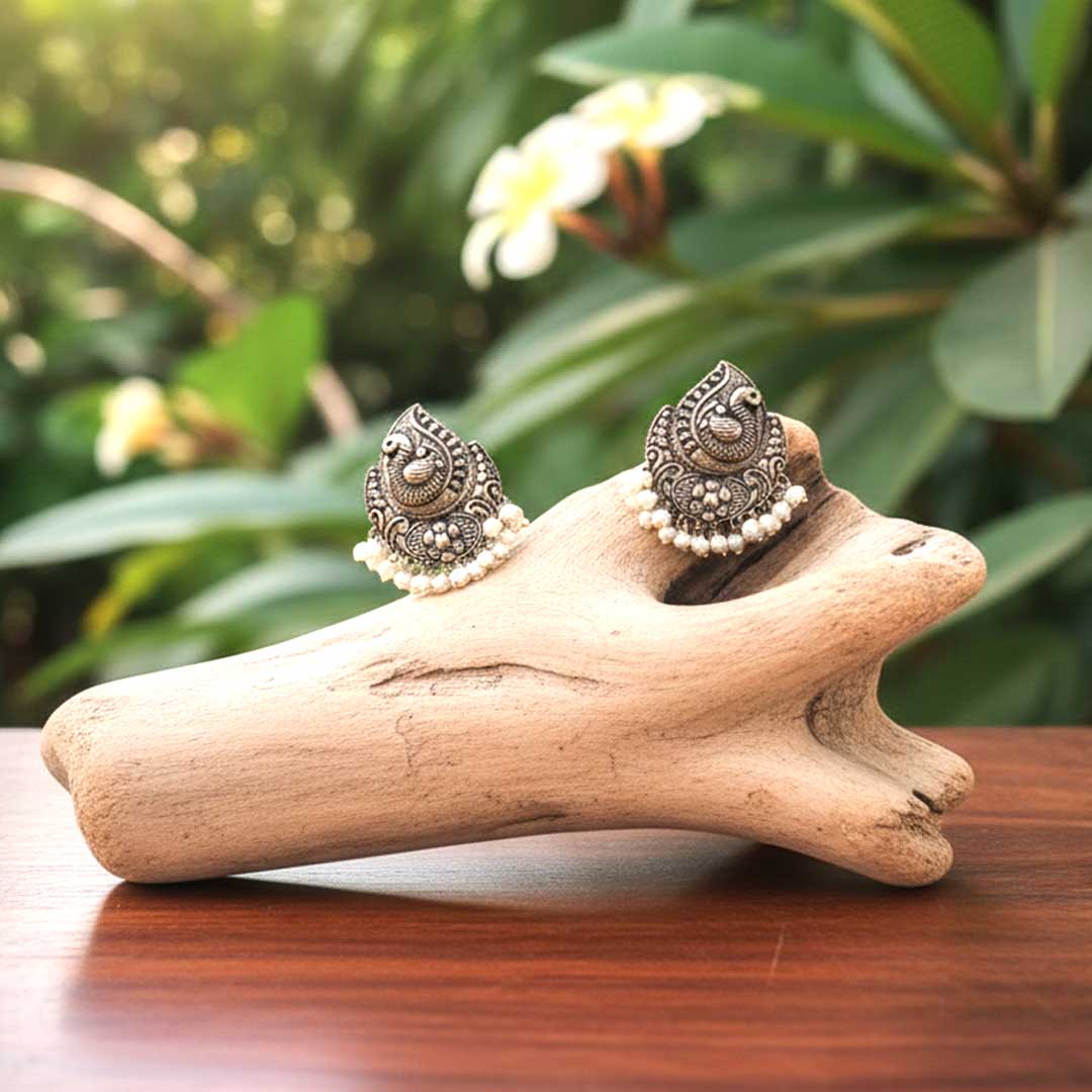 Pair of ornate earrings on a piece of driftwood with a natural background
