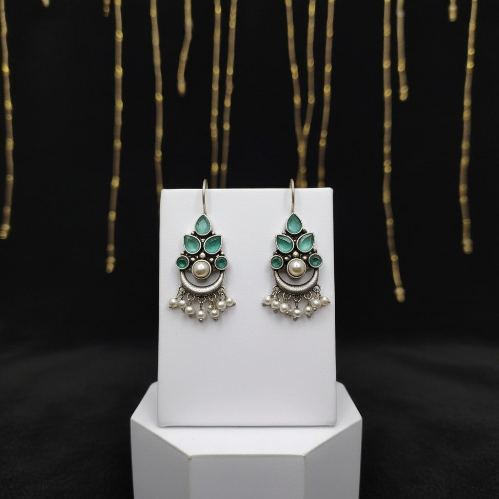 Pair of silver earrings with green gemstones on a white stand against a black background with gold accents.