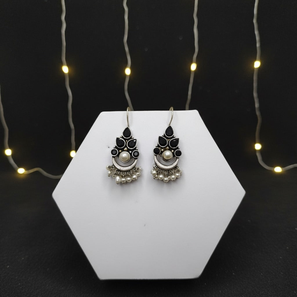 Pair of earrings on a hexagonal white stand with string lights in the background