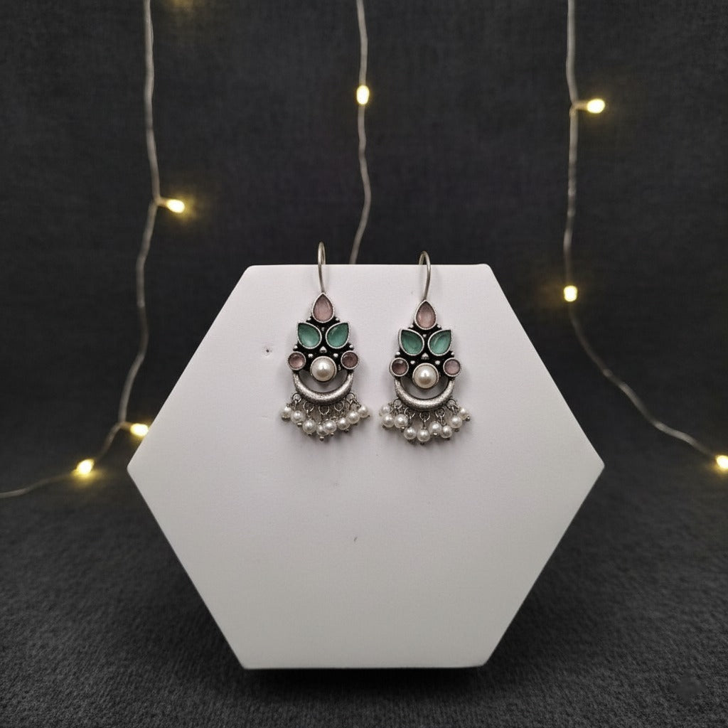 Pair of earrings on a white hexagonal stand with a dark background and string lights.
