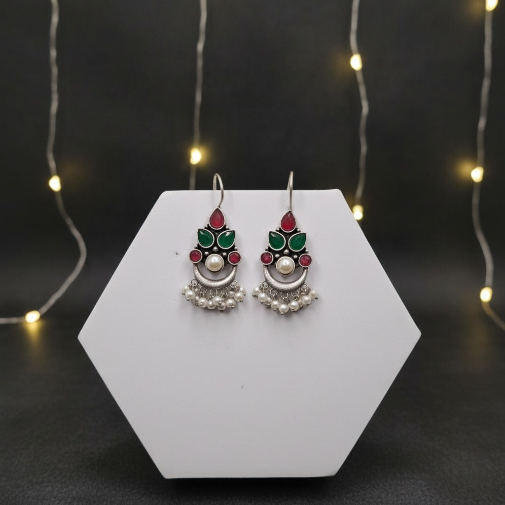 Decorative earrings on a white hexagonal stand with a dark background and string lights.