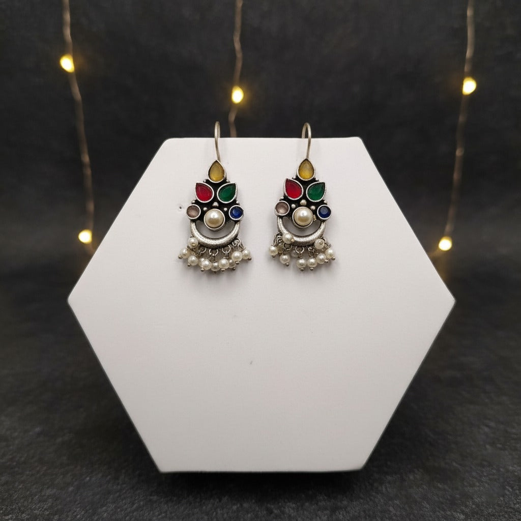 Decorative earrings on a white hexagonal stand with a dark background and string lights.