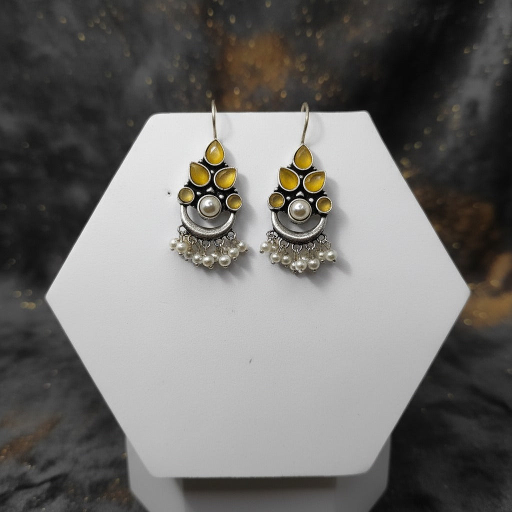 Pair of earrings on a white hexagonal stand with a dark background