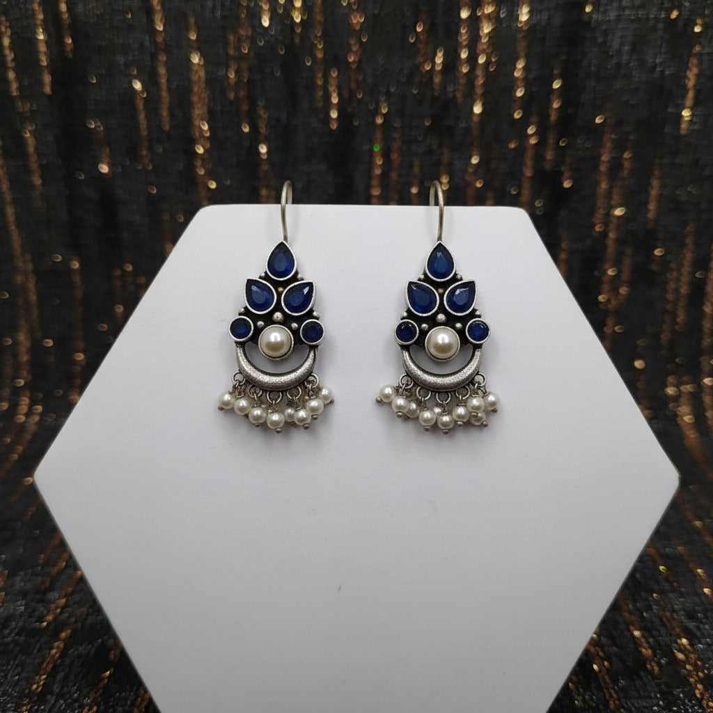 Pair of earrings on a white hexagonal stand with a dark, textured background