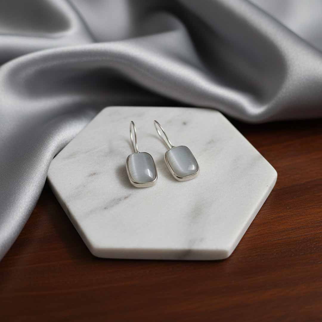 Silver earrings with blue stones on a marble stand with gray fabric in the background