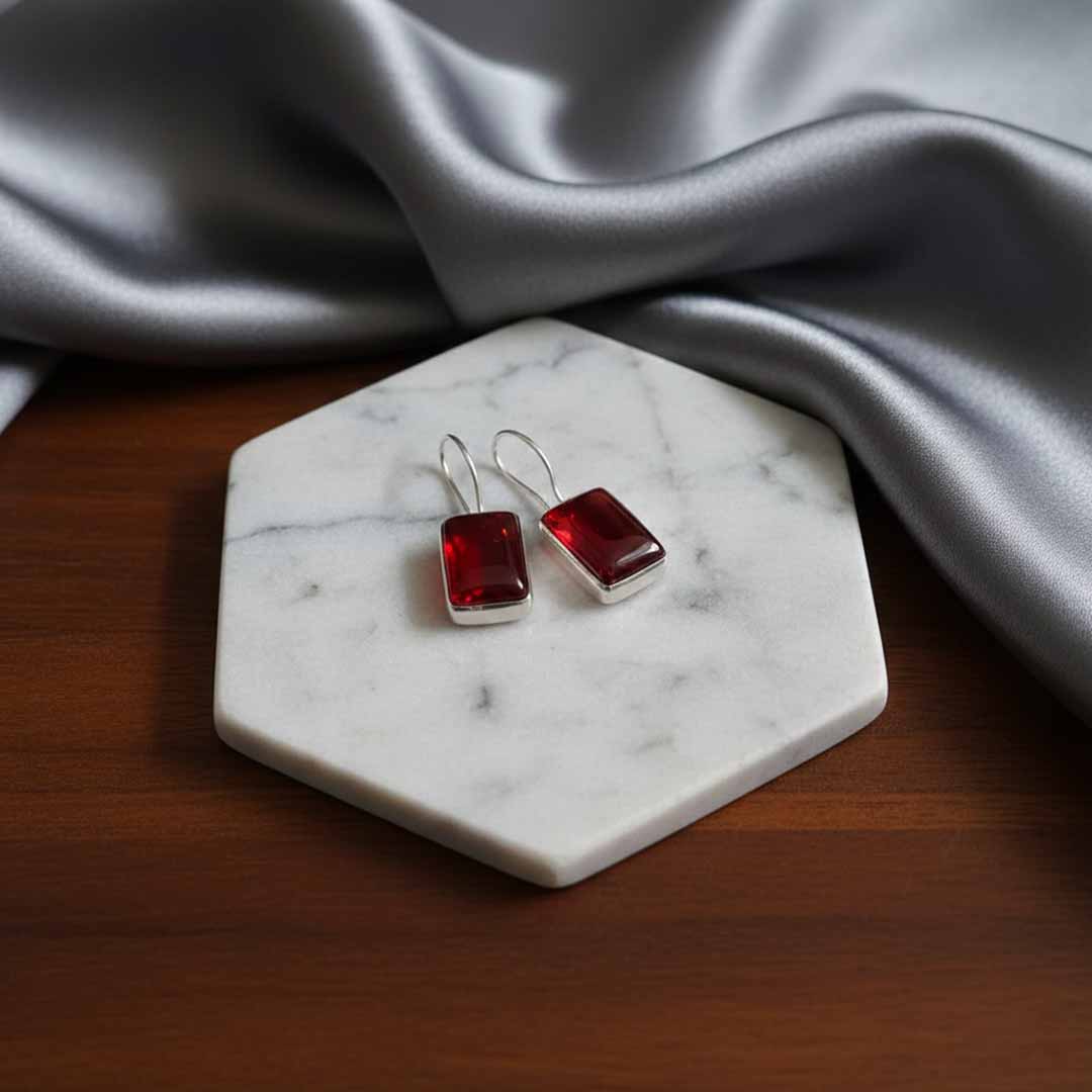 Red square earrings on a marble stand with gray fabric in the background