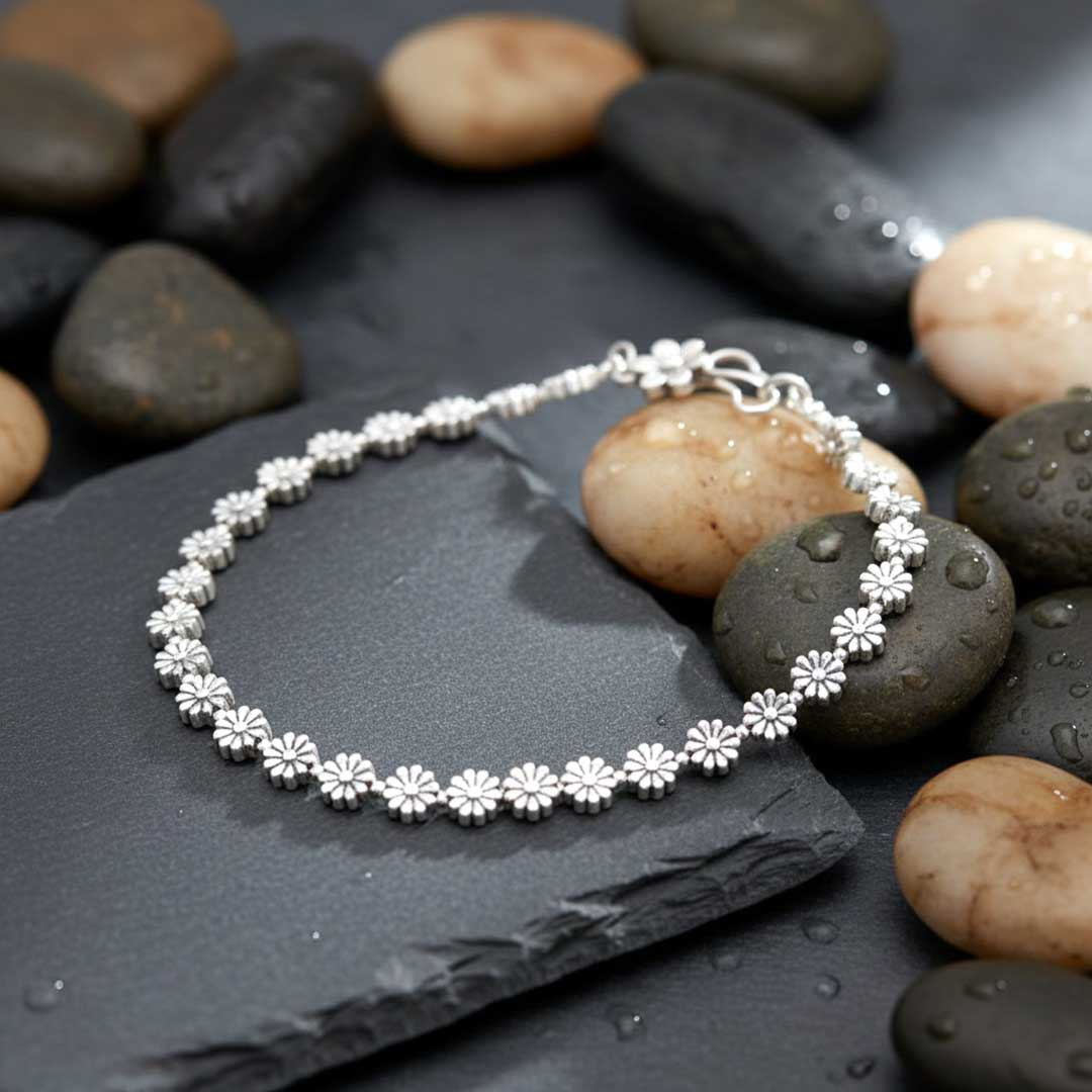 Silver bracelet on a dark stone surface with pebbles in the background