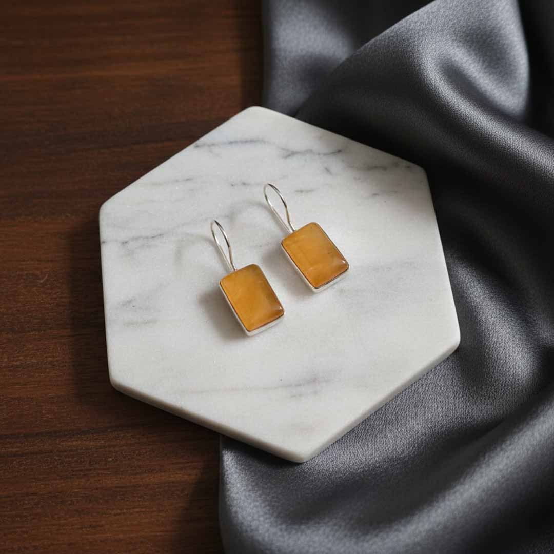 Square yellow earrings on a marble coaster with gray fabric background