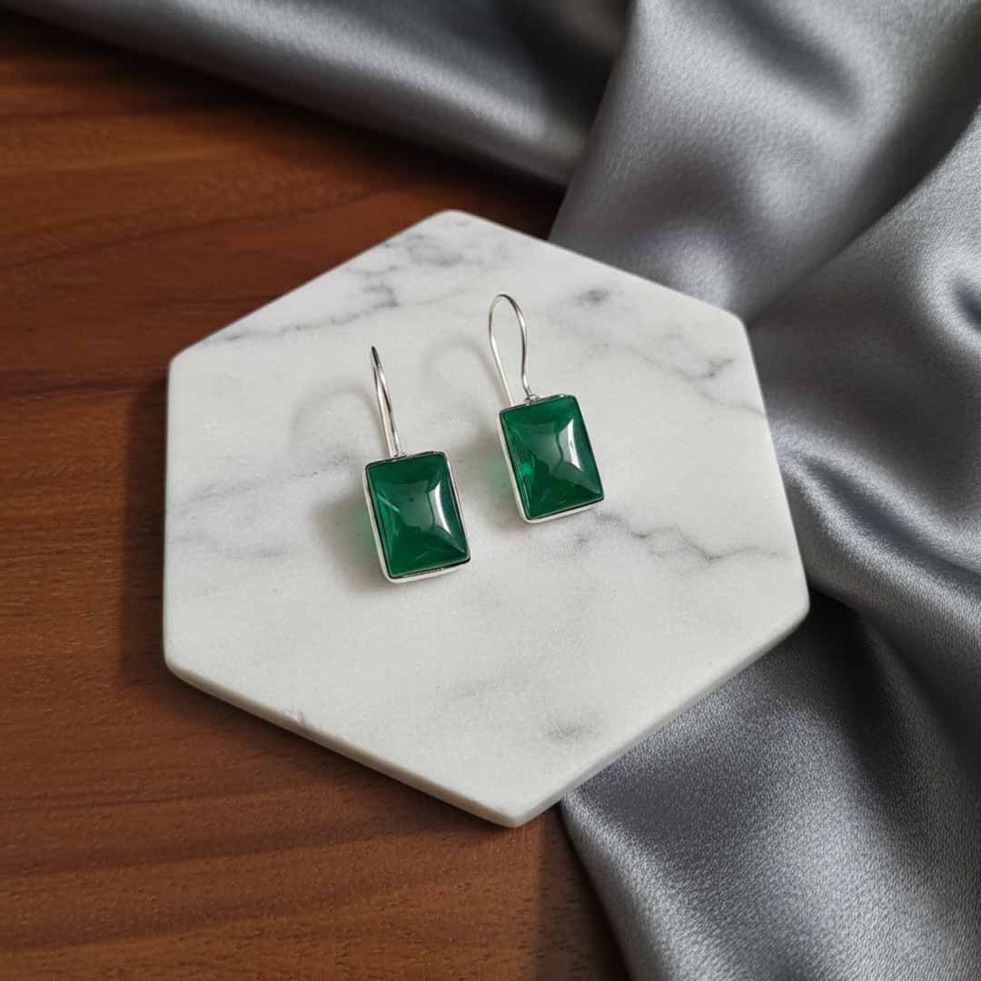 Green square earrings on a marble coaster with gray fabric in the background