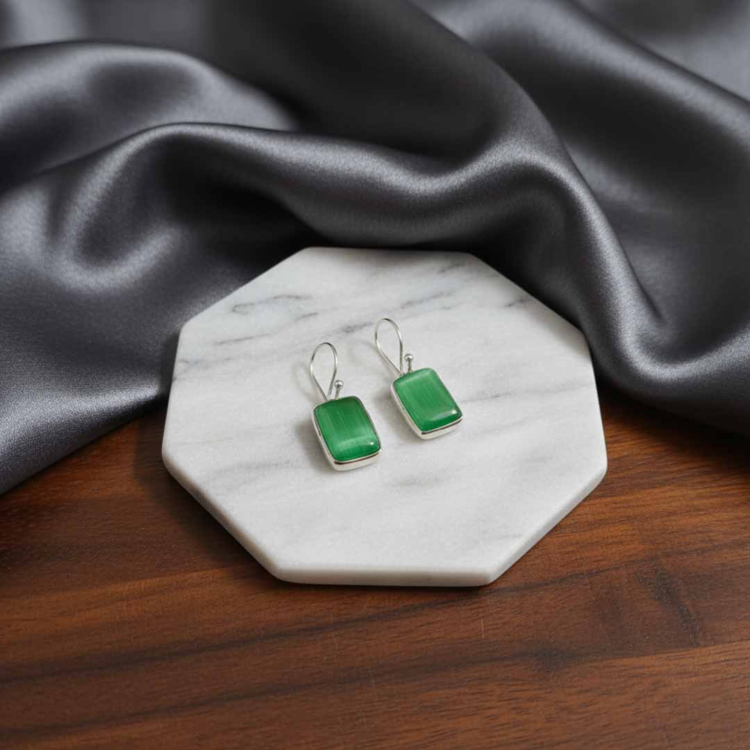 Green square earrings on a marble stand with gray fabric in the background